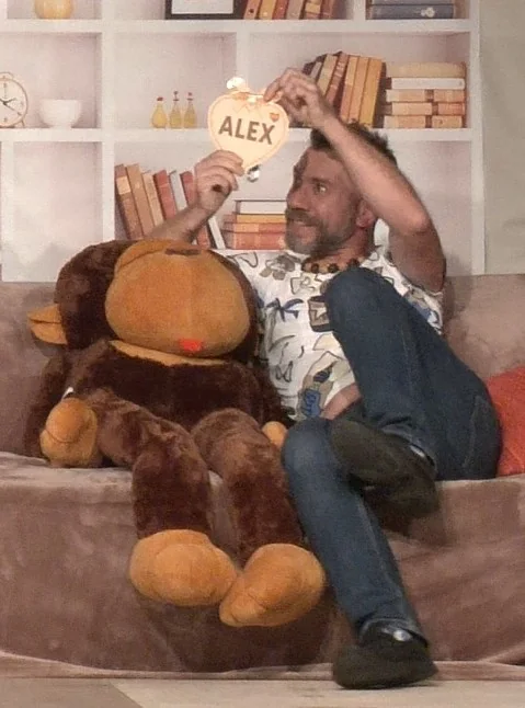 Benjamin assis sur le canapé avec le singe en peluche et un panneau portant le prénom Alex