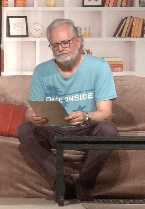 Chris assis sur scène, lisant une lettre conservée dans sa boîte de correspondance