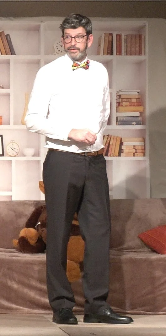 Jean-Luc debout sur scène, en chemise blanche et nœud papillon, dans une attitude réservée